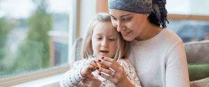 mother with cancer wearing a head scarf playing with young daughter