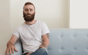 Man with beard and tattoos sitting on a sofa looking serious
