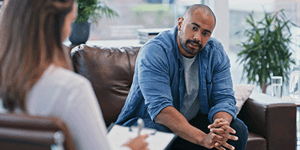 man sitting on a sofa talking to a female counsellor who is seated opposite