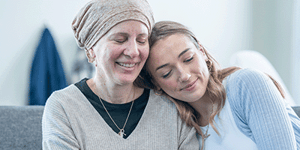 daughter resting her head on mother's shoulder mother has cancer and is wearing a headscarf
